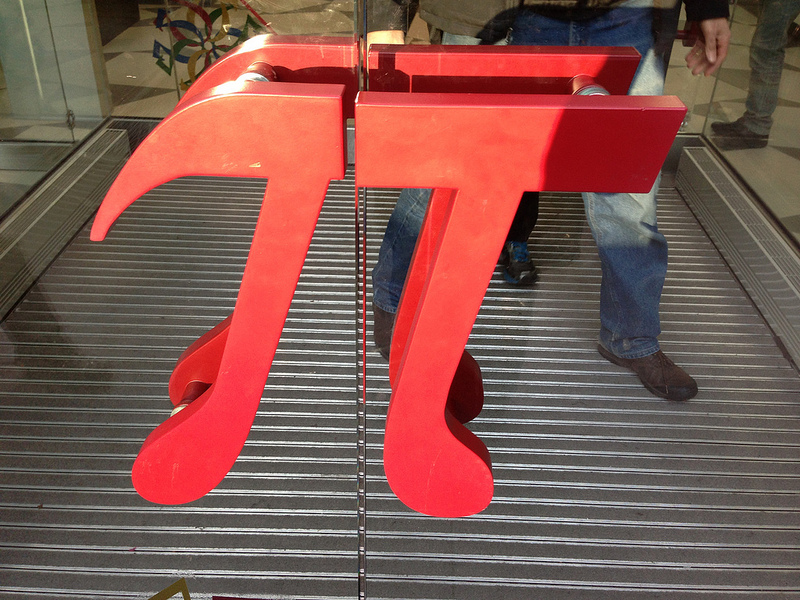 Símbolo Pi en metal rojo que, dividido a la mitad, sirve de tiradores para las dos hojas de una puerta de cristal