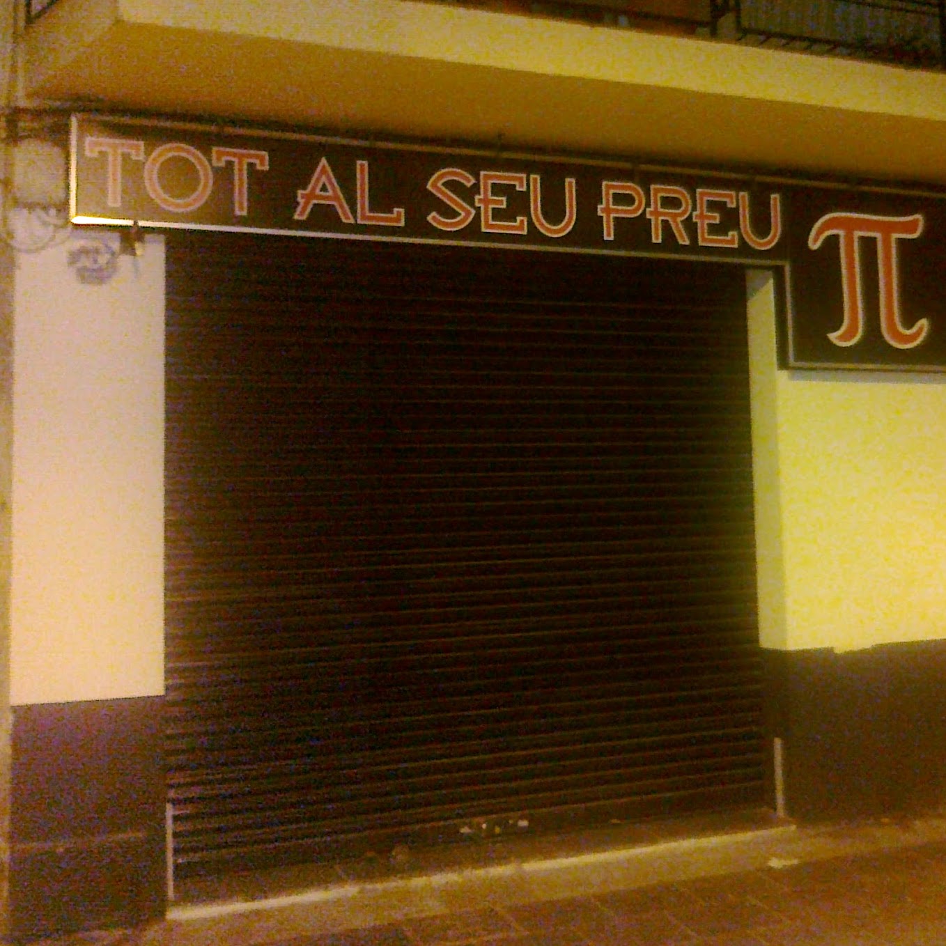 Persiana cerrada de una tienda, cuyo cartel dice Tot al seu preu - Pi (con el símbolo griego)